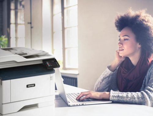 Joven trabajando en su ordenador junto a una impresora multifunción Xerox® B315.