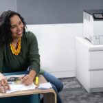 Mujer sonriente en una oficina junto a la impresora a color Xerox® VersaLink® C620