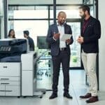 Dos hombres en una oficina conversan sobre algo en una tableta junto a una impresora multifunción en color Xerox® AltaLink® C8200 Series Dos hombres en una oficina conversan sobre algo en una tableta junto a una impresora multifunción en color Xerox® AltaLink® C8200 Series