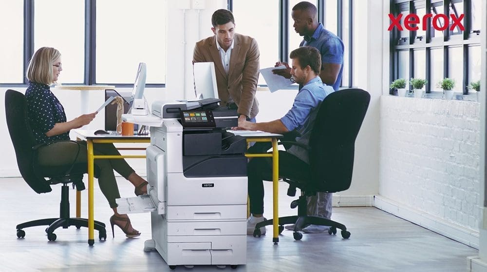 Trabajadores de oficina colaborando cerca de una impresora Xerox.