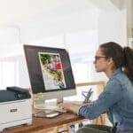 Una mujer sentada en un escritorio, concentrada en su trabajo, con una impresora Xerox® C320 a color Una mujer sentada en un escritorio, concentrada en su trabajo, con una impresora Xerox® C320 a color