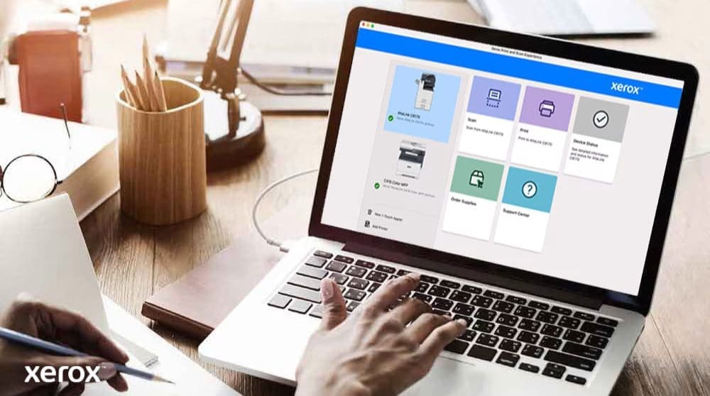 Experiencia de impresión y escaneo de Xerox®: control intuitivo Las manos de una persona están sobre el teclado de una computadora portátil y la pantalla muestra la interfaz de Xerox Print and Scan Experience con opciones como Escanear, Imprimir, Estado del dispositivo, Solicitar suministros y Centro de soporte, lo que indica un control fácil de usar.