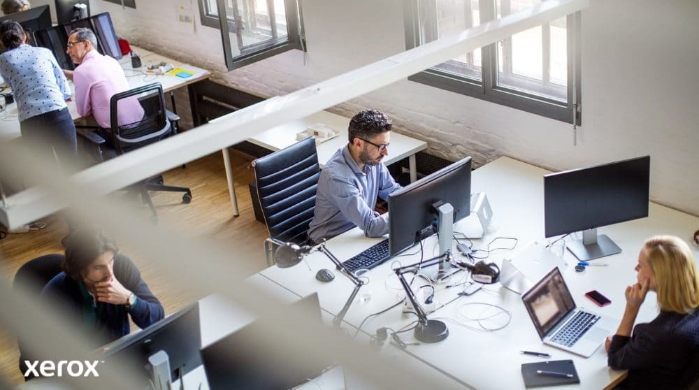 Experiencia de impresión y escaneo de Xerox®: Impulsando la productividad en la oficina Vista aérea de una oficina diáfana con varias personas trabajando en sus escritorios y usando computadoras. La escena transmite un ambiente de trabajo productivo y colaborativo.