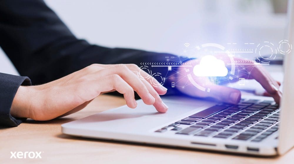 Xerox® Workplace Cloud y Suite: Conectividad en la nube Se muestran las manos de una persona escribiendo en el teclado de una computadora portátil, con un ícono de nube brillante y conexiones de red superpuestas sobre la imagen, simbolizando la conectividad en la nube y los flujos de trabajo digitales.