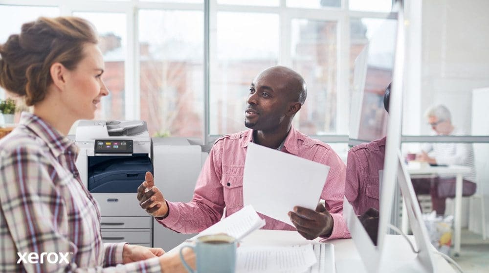 Xerox® Workplace Cloud y Suite: Gestión centralizada de flotas Una persona revisa datos en la pantalla de una computadora portátil, con una superposición digital de varios íconos de dispositivos (impresoras, dispositivos móviles) y líneas conectadas, que simbolizan la gestión centralizada de la flota para Xerox Workplace Solutions.